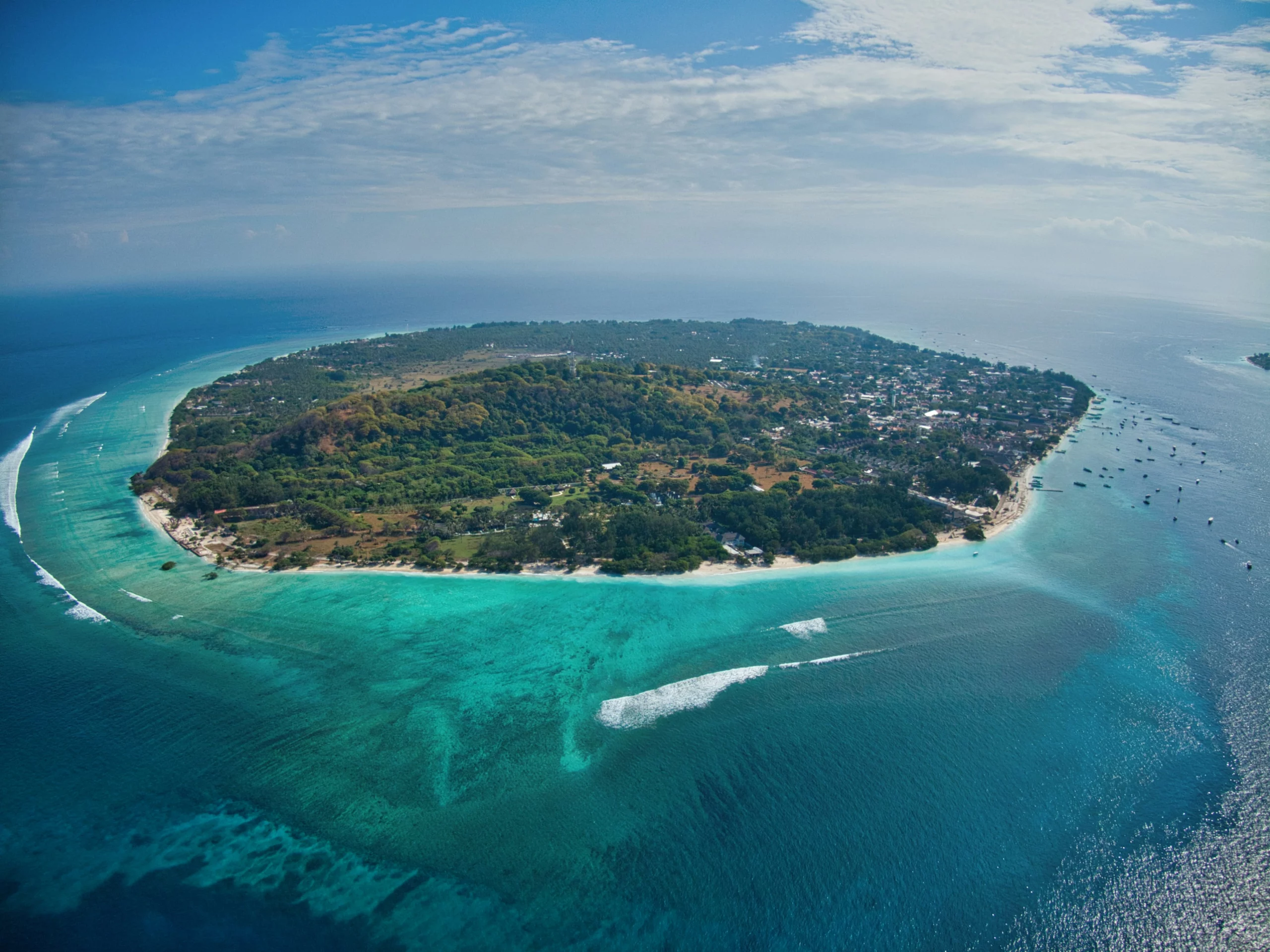 Voyage entre femmes en Indonésie : vue aérienne d’une île tropicale entourée d’eaux turquoise et de coraux avec bateaux ancrés – Salma Travel