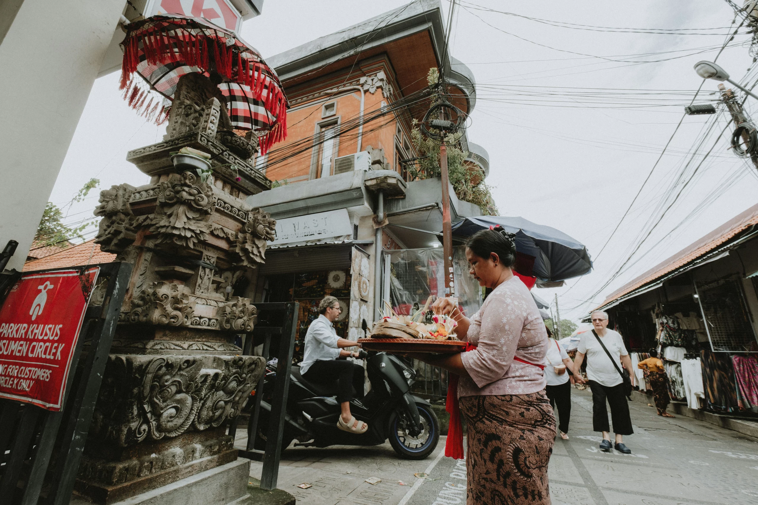 Voyage entre femmes en Indonésie : femme balinaise portant une offrande dans une rue avec sculptures traditionnelles – Salma Travel