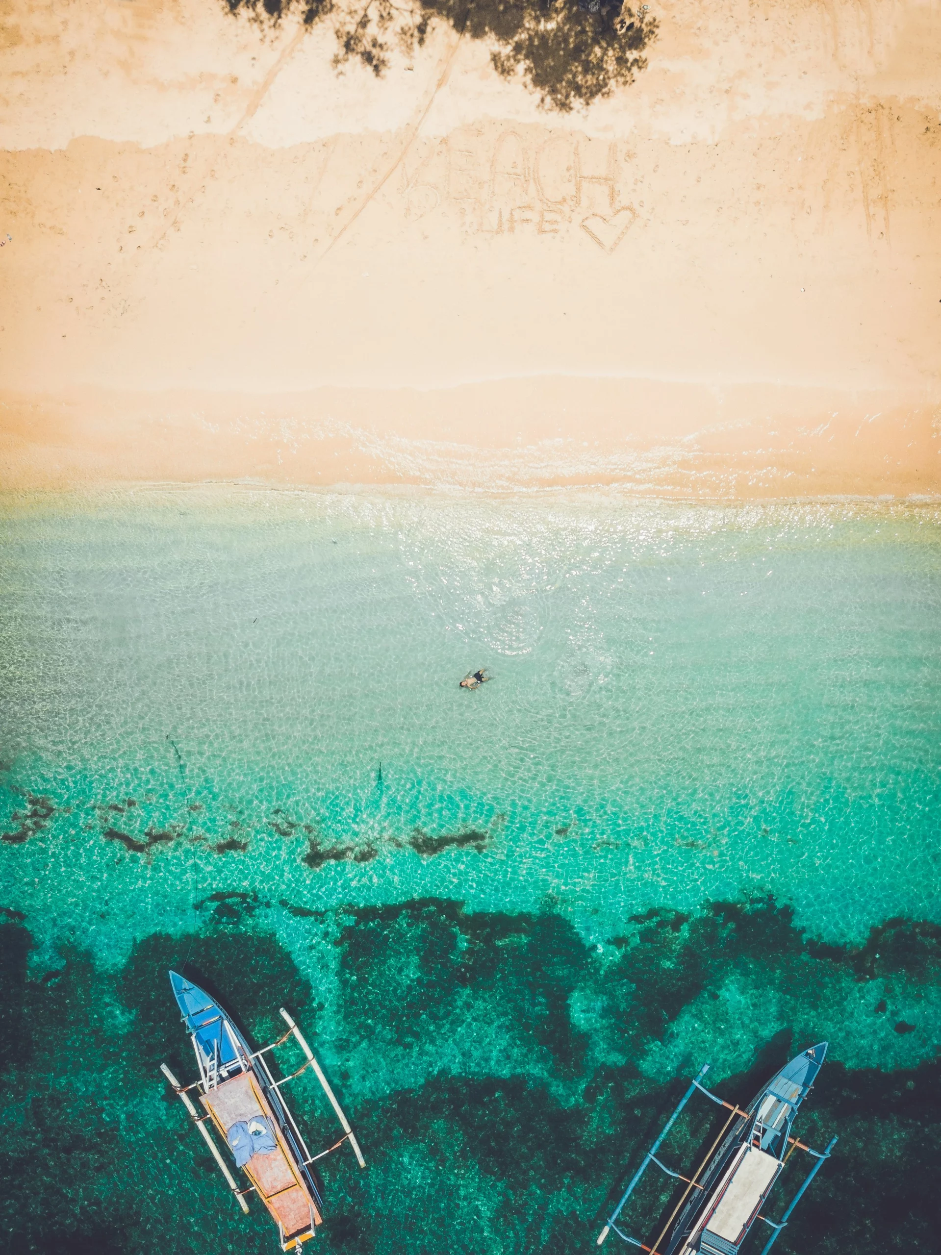 Voyage entre femmes en Indonésie : vue aérienne d’une plage de sable clair, mer turquoise et bateaux traditionnels – Salma Travel