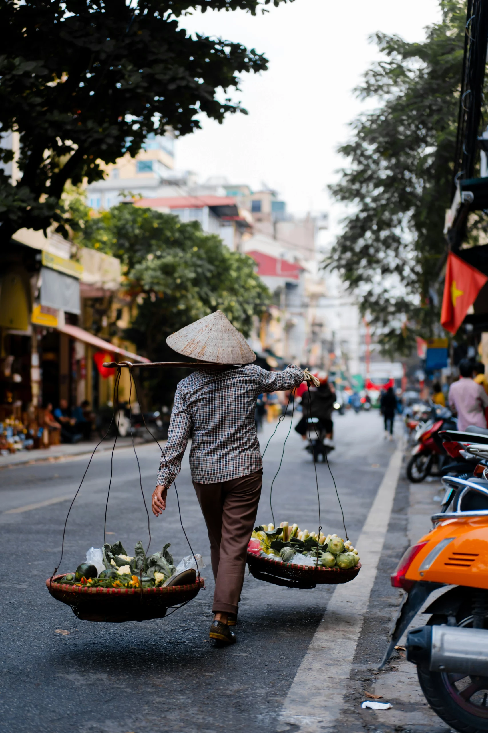 Voyage entre femmes au Vietnam : marchande ambulante à Hanoï portant des paniers de fruits sur un bâton dans une rue animée – Salma Travel