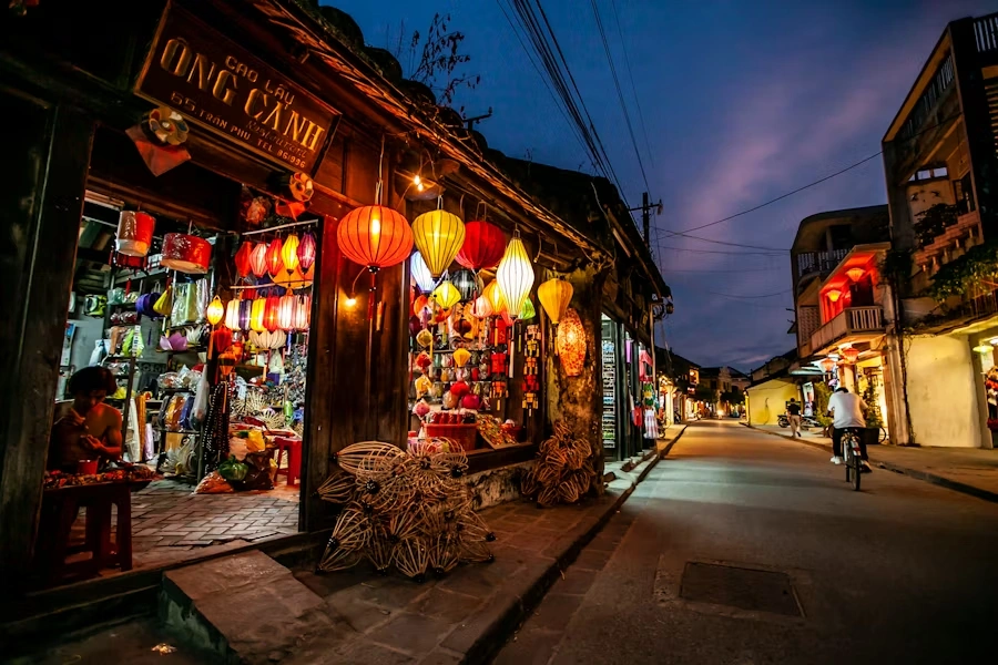 Voyage entre femmes au Vietnam : ruelle de Hoi An illuminée de lanternes colorées avec boutique d’artisanat et cycliste de nuit – Salma Travel