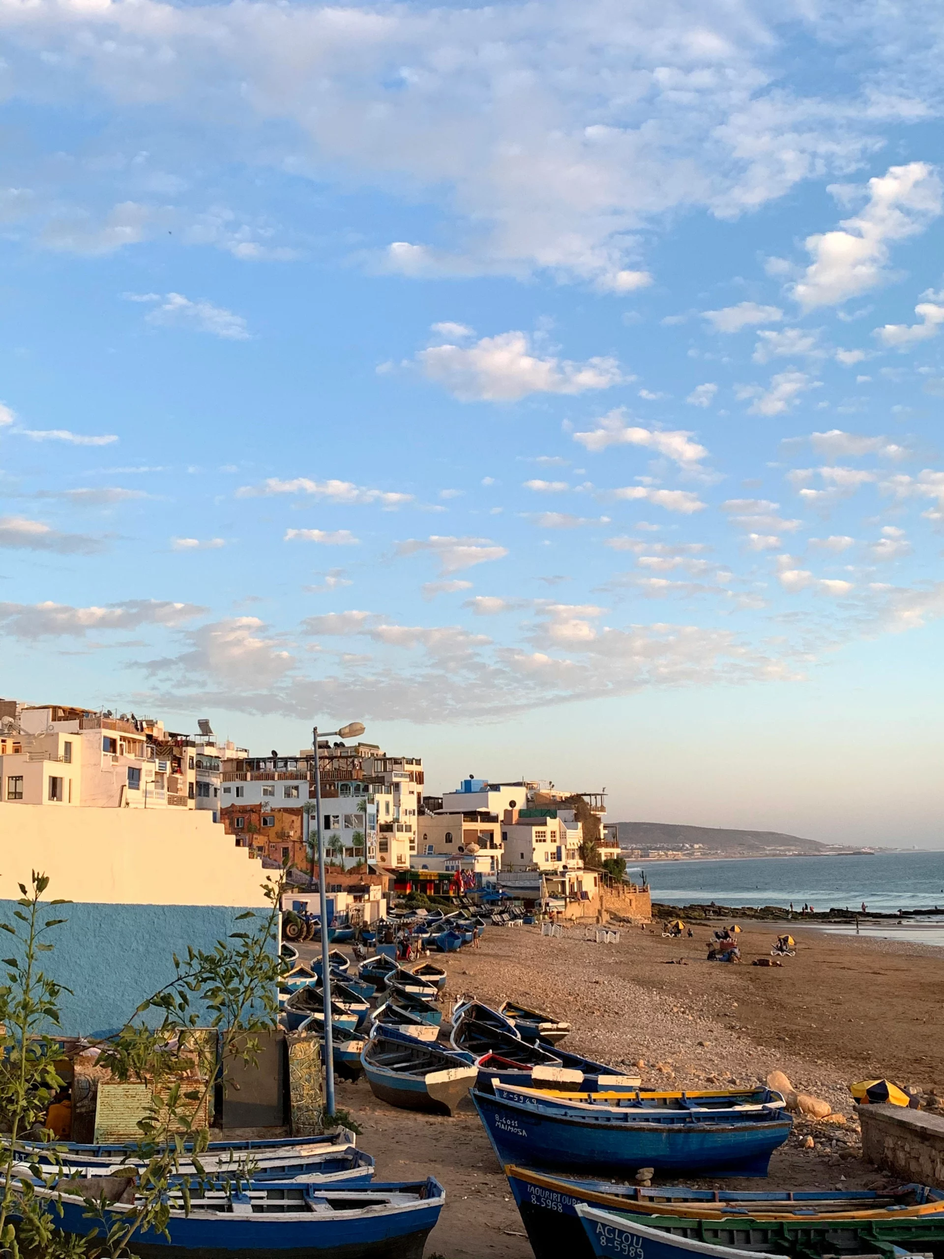 Voyage entre femmes au Maroc : plage avec barques de pêche et village côtier au coucher du soleil – Salma Travel